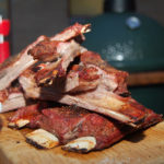 Im Vordergrund sind gegrillte Spareribs zu sehen, im Hintergrund einer der besten Keramikgrills: Der Big Green Egg XLARGE.