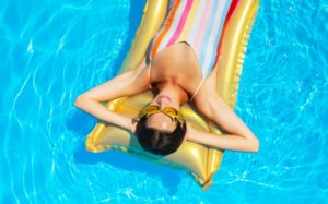 Frau schwimmt mit einer Luftmatratze auf dem Wasser ihres Aufstellpools.