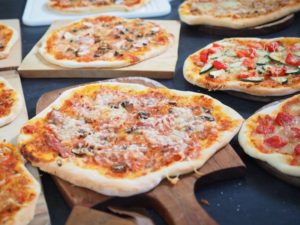 Mehrere Pizzen auf Pizzasteinen und eine Pizza auf einem Pizzaschieber