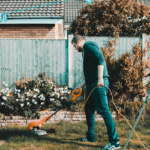 Ein Mann der mit einem Elektro-Rasentrimmer im Garten arbeitet.