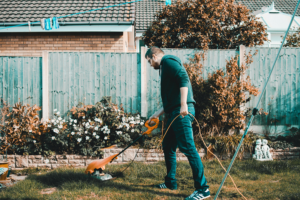 Ein Mann der mit einem Elektro-Rasentrimmer im Garten arbeitet.