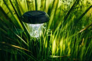 Ein einzelner Gartenstrahler steht im Gras und gibt Licht ab.